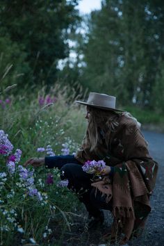 a woman kneeling down in the middle of a field with purple and white flowers next to her