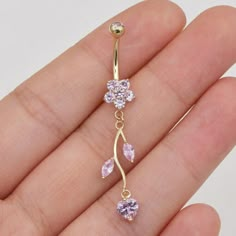 a close up of a person's hand holding a gold belly ring with pink stones