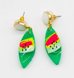 two pairs of green and yellow earrings on a white surface, one with a painted leaf