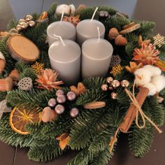 three candles are sitting in a wreath with decorations around it on a table top, surrounded by pine branches and oranges