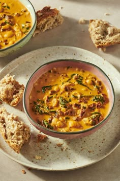 a bowl of soup on a plate next to two pieces of biscuits and bread