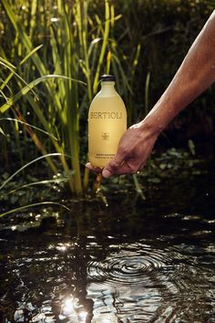 a person holding onto a bottle that is in the water with grass and plants behind it