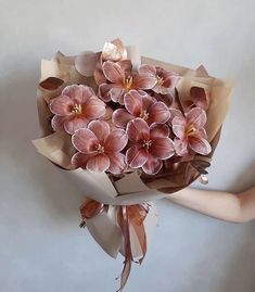 a person holding a bouquet of flowers with brown paper wrapped around it's stems