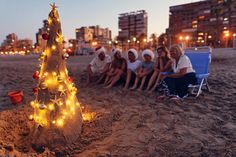 a group of people sitting on top of a sandy beach next to a christmas tree