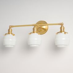 three light brass bathroom fixture with white glass shades on the arms and bottom lights, against a plain background