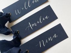 three black name tags with white writing on them, one has a blue ribbon tied around it