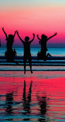 three people jumping into the air on a beach at sunset with their arms in the air