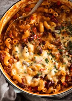 a skillet filled with pasta and cheese on top of a cloth next to a spoon