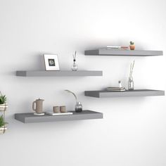 three floating shelves with plants and vases on them against a white wall in a room