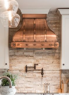 a kitchen with white cabinets and a copper range hood over the sink in front of an oven