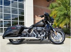 a black motorcycle is parked in front of a building with palm trees and large windows