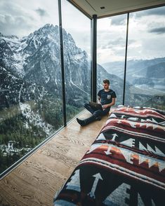 a man sitting on top of a bed in front of a window next to a mountain