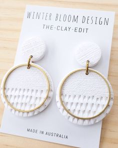 a pair of white and gold earrings sitting on top of a wooden table next to a card