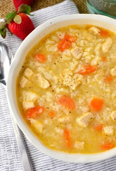 a white bowl filled with chicken and rice soup next to strawberries on a table