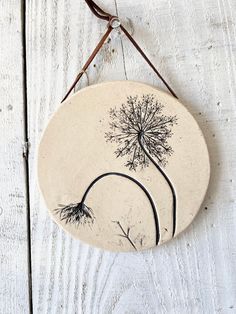 a ceramic wall hanging with a dandelion design on it's side and brown leather cord