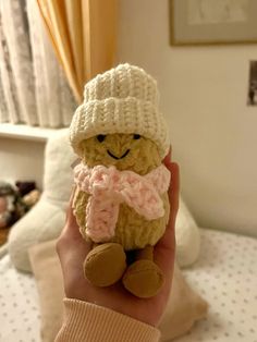 a hand holding a small teddy bear wearing a knitted hat and scarf