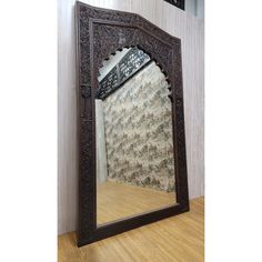 an ornately carved mirror is on the floor in front of a wallpapered wall