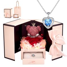 a teddy bear in a gift box surrounded by other items such as a necklace, ring and bag