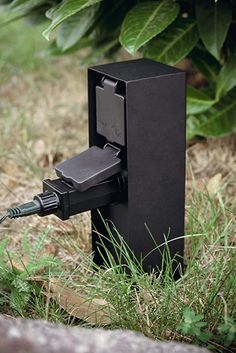 an electronic device is plugged in to the ground by some grass and bushes,