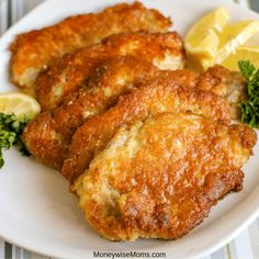 some fried food on a white plate with lemon wedges and parsley