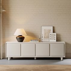 a white sideboard with a lamp and pictures on it in front of a brick wall