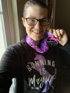 a woman holding up a medal in front of her face with the words running is magic on it