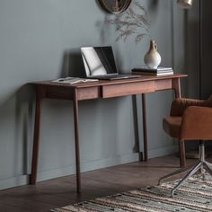 a laptop computer sitting on top of a wooden desk next to a vase with flowers