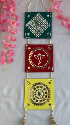 three colorful cards with designs on them and tassels hanging from the strings next to pink flowers