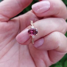 a woman's hand holding a ring with a red stone in it