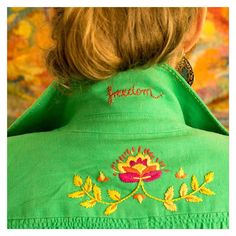 the back of a woman's green jacket with embroidered flowers on it and name written in red