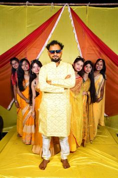 a man standing in front of a group of women wearing yellow and orange sari