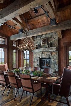 a dining room table with chairs and a chandelier hanging from the ceiling in front of a stone fireplace