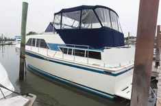 a white boat docked at a dock with other boats in the water and one is blue