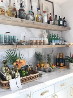 a kitchen counter filled with lots of bottles and glasses on top of wooden shelves next to white cabinets