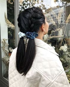 a woman standing in front of a window wearing a white jacket and blue flower clip