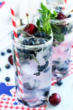 two glasses filled with ice and cherries on top of a red white and blue checkered table cloth