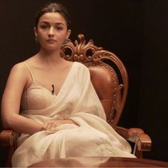 a woman sitting in a chair wearing a white sari and looking at the camera