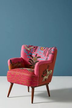 a pink chair sitting on top of a white floor next to a blue wall and wooden legs