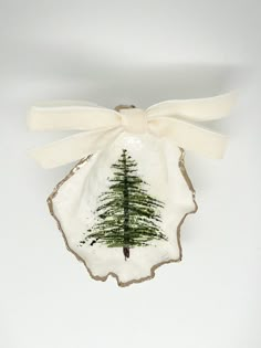 a ceramic ornament with a pine tree on it's side and a white ribbon tied around the edge