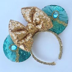 two blue and gold minnie mouse ears with sequins on the ears, one has a large bow