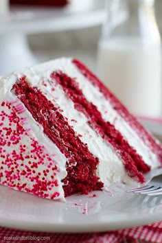 a slice of red velvet cake with white frosting and sprinkles on a plate