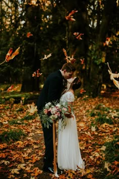 a bride and groom kissing in the woods surrounded by autumn leaves, with butterflies flying overhead