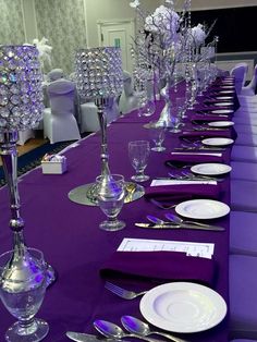 the table is set with purple linens and place settings for an elegant dinner party