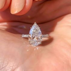 a woman's hand holding an engagement ring with a pear shaped diamond