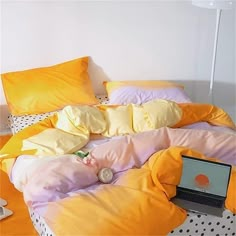 a laptop computer sitting on top of a bed covered in yellow and pink sheets with polka dots