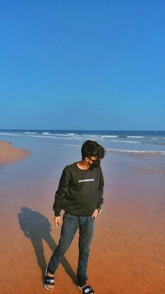 a man standing on top of a sandy beach next to the ocean with his shadow