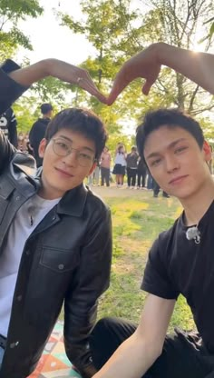 two young men sitting next to each other on top of a blanket in a park