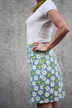 a woman wearing a white shirt and blue flowered skirt with her hands on her hips