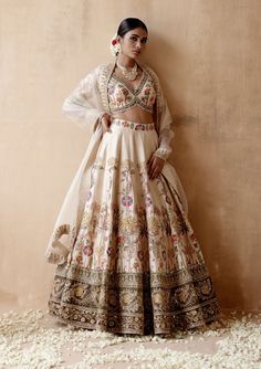 Editor's Note Presenting an opulent ivory raw silk lehenga set adorned with intricate floral thread embroidery and sumptuous velvet patchwork, elegantly highlighted with various embellishments. This captivating ensemble is paired with an embroidered blouse and dupatta, creating a regal and luxurious look perfect for grand occasions or elegant gatherings. The combination of the rich raw silk texture, the exquisite embroidery, and the ornate details on both the blouse and dupatta add a touch of op Motifs For Embroidery, Floral Embroidery Lehenga, White Wedding Lehenga, Ipl Videos, Sharara Style, Floral Thread Embroidery, Indian Fits, Embroidery Lehenga, Velvet Patchwork