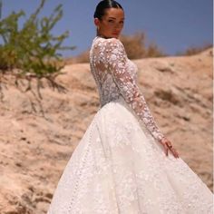 a woman in a wedding dress standing on top of a hill with her hand on her hip